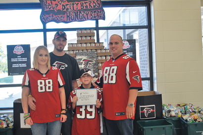 WCES Principal, Steven Rouse with student Matthew Rooks and his parents as Matthew receives a thank you note and jersey from the Atlanta Falcons for his hard work on collecting hundreds of cans of food for the FalCan food drive.